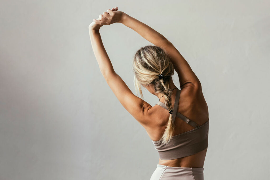a woman with blond hair in yoga clothes stretches to the side.