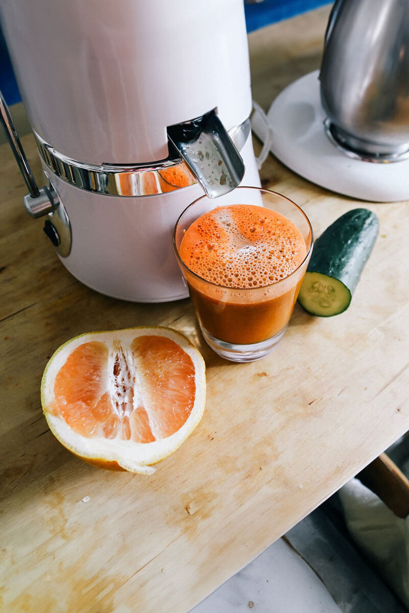 a juicer pours orange juice into a cup. half of an orange and a cucumber is on the table