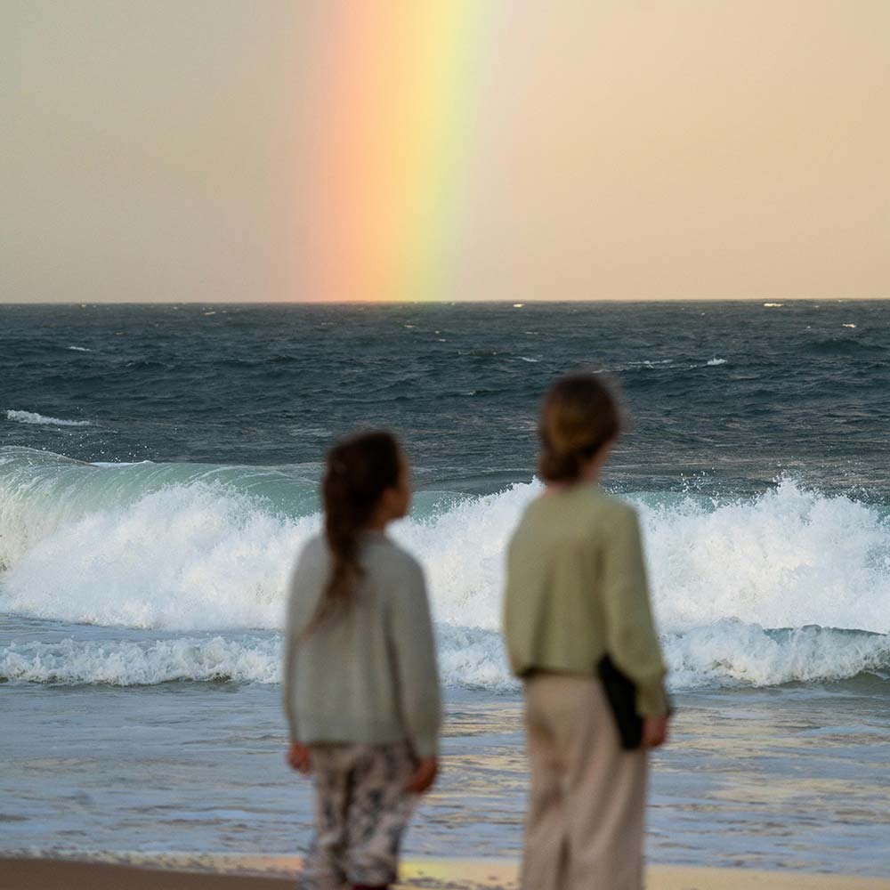 Two sisters looking at a rainbow over the ocean