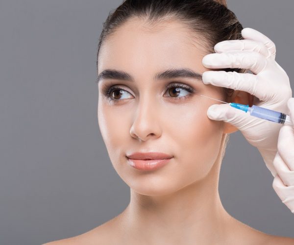 Portrait of attractive young woman making cosmetic injections Women face care. Portrait of attractive young woman making cosmetic injections on grey background, closeup, empty space