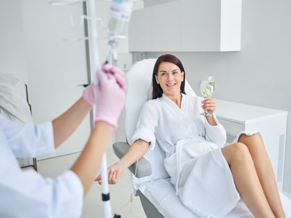 Smiling pleased female patient with a glass of healthy drink sitting in a cosmetic chair